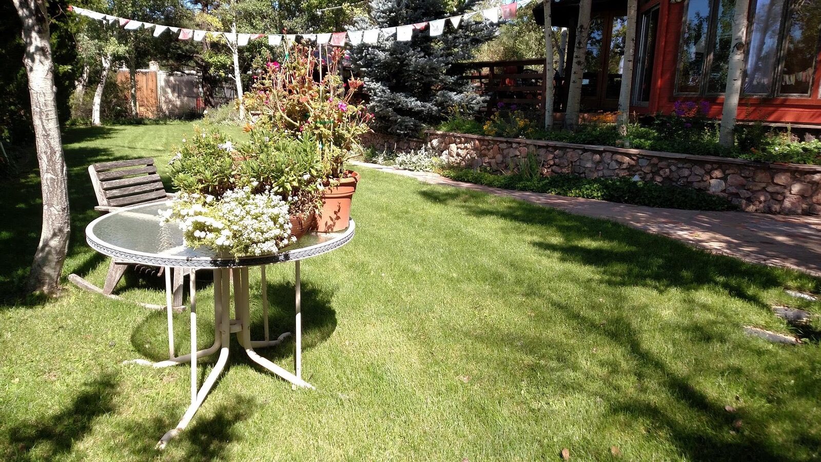 A wide view of the garden — lawn, stone wall, aspen trees, prayer flags strung overhead
