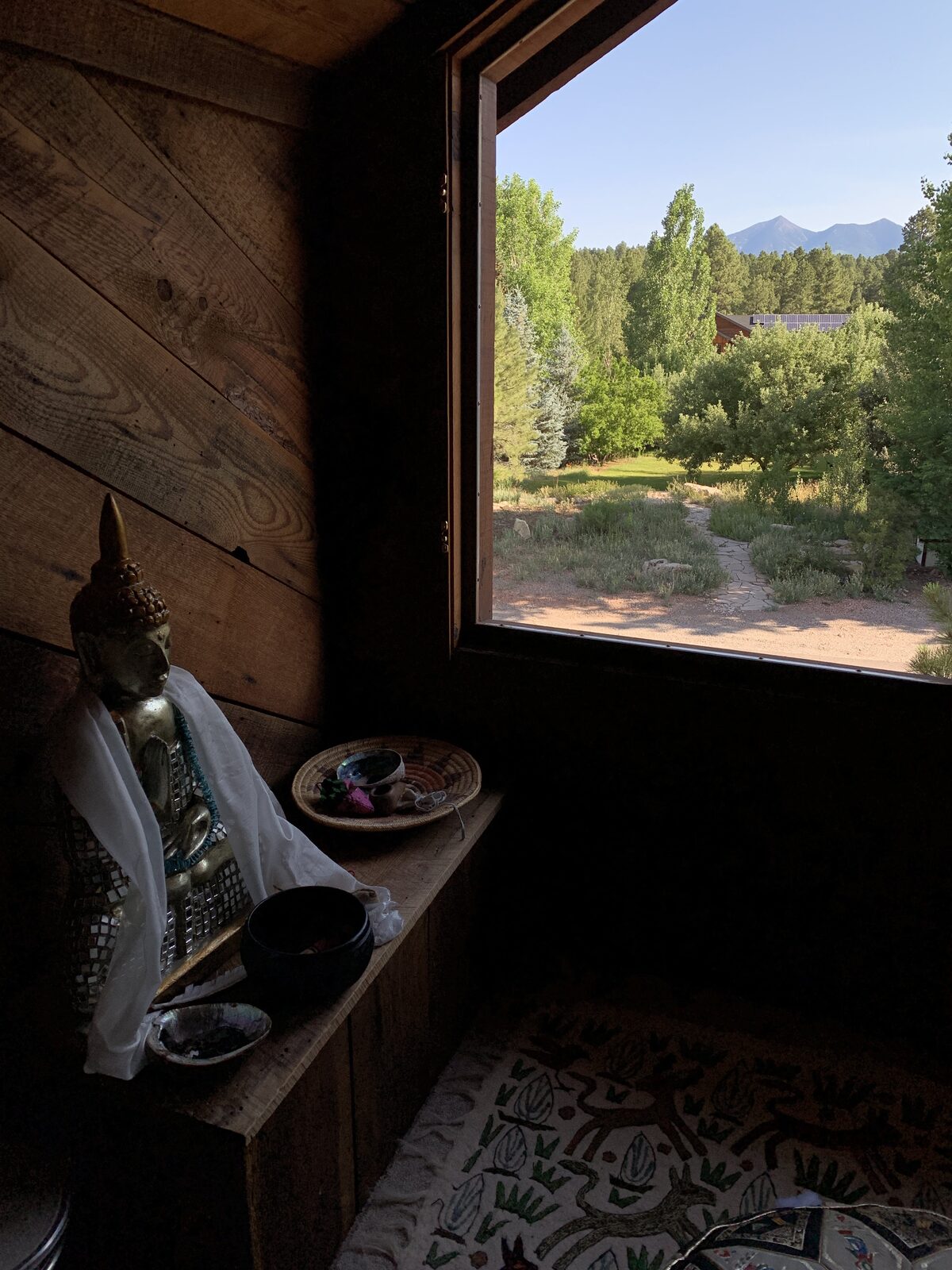 A meditation room's window framing a distant sacred mountain, a golden Buddha on the altar